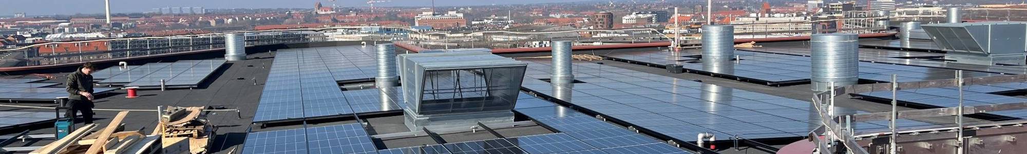 Solpaneler på tag med udsigt over byen og klart blå himmel